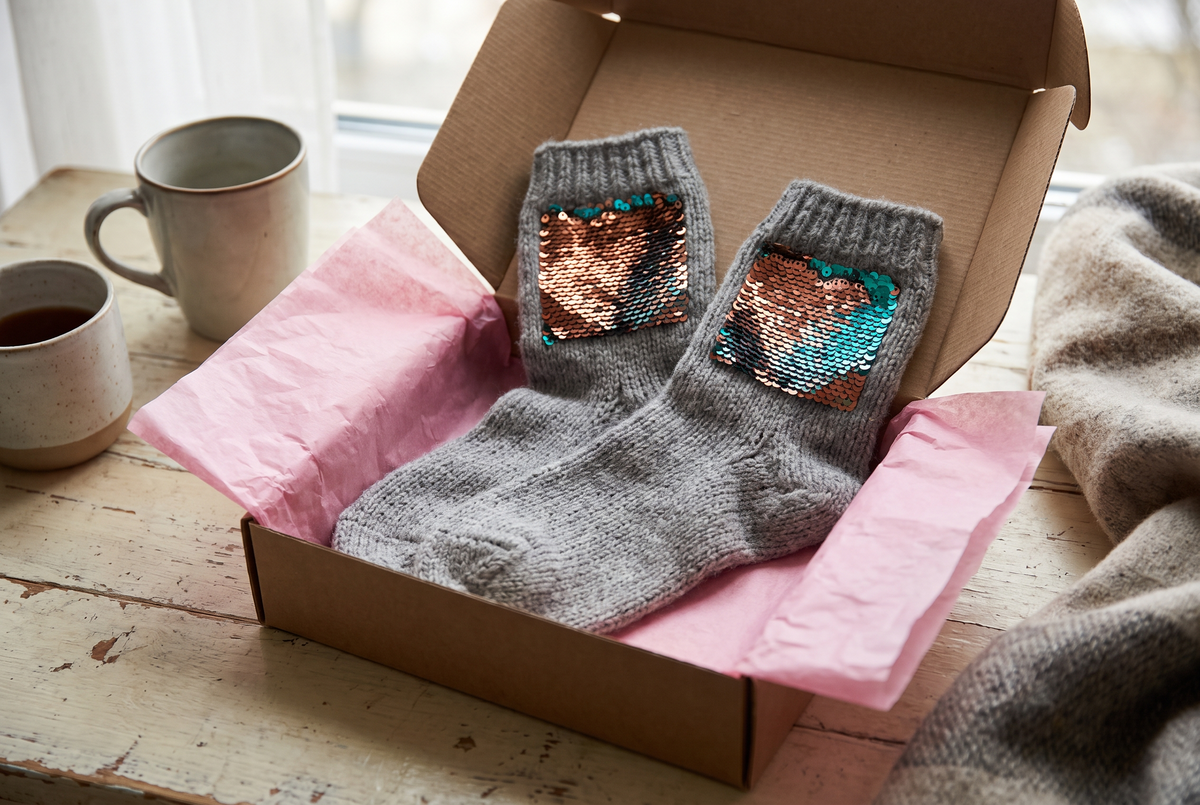 Paire de chaussettes à paillettes réversibles posée dans une boîte cadeau ouverte avec du papier de soie Image