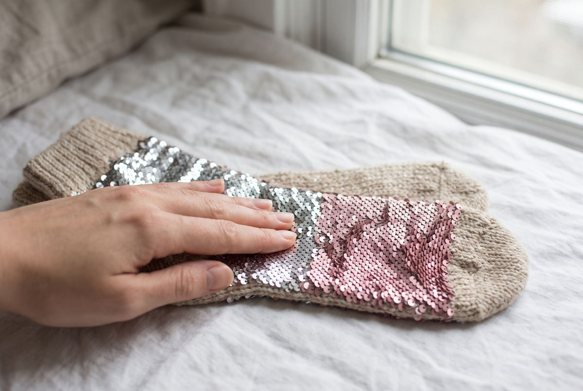 Main qui brosse les paillettes réversibles d'une chaussette posée sur un lit, les paillettes changeant de couleur sous le doigt Image
