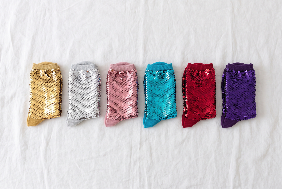 Plusieurs paires de chaussettes à paillettes de couleurs variées alignées sur un drap blanc